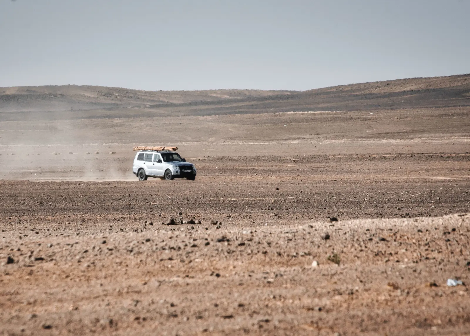 4x4 sur une piste de plateau aride 4x4 blanc roulant sur une piste caillouteuse à travers un vaste plateau aride