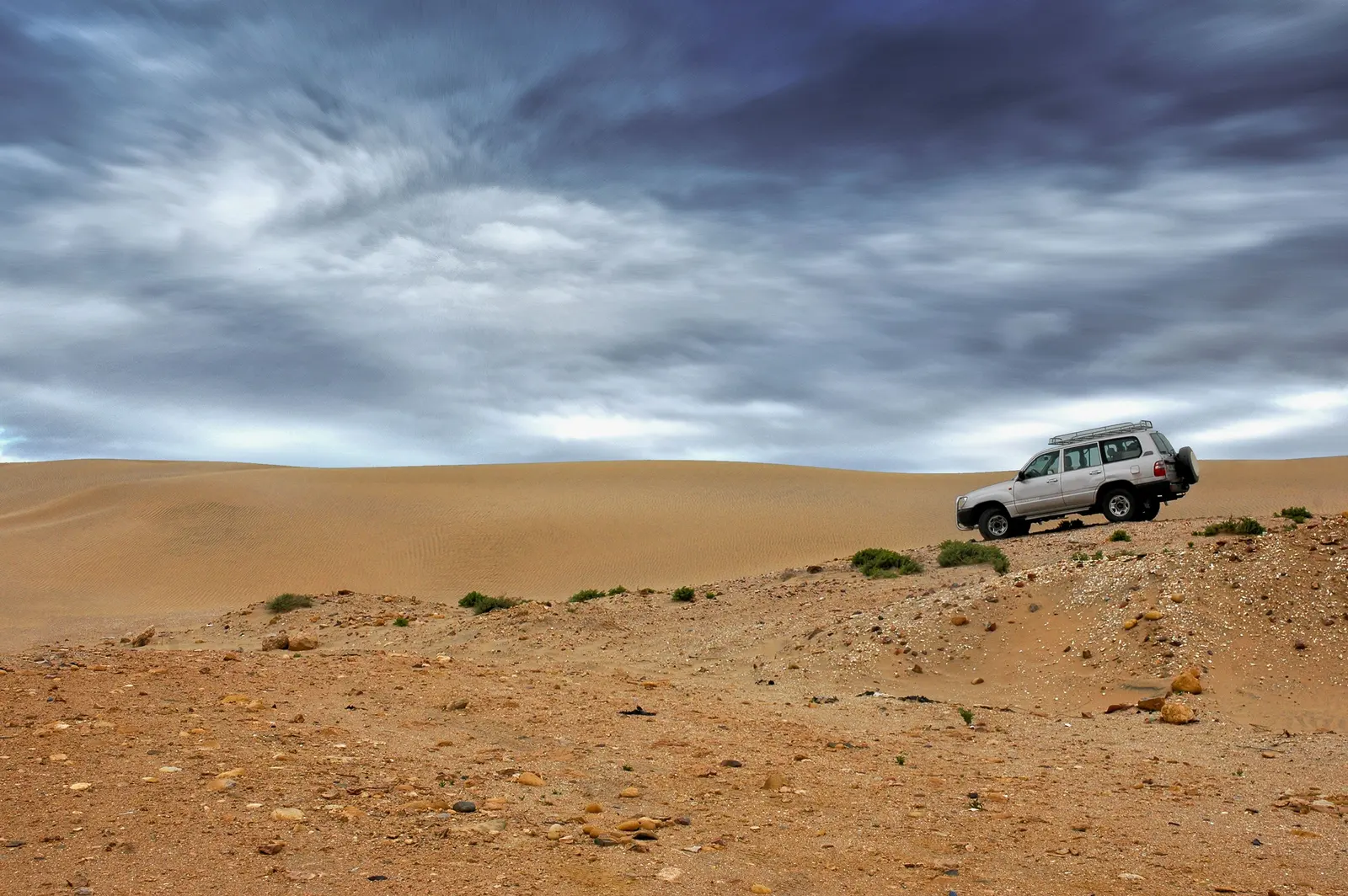 4x4 blanc sur un terrain désertique rocheux sous un ciel chargé de nuages