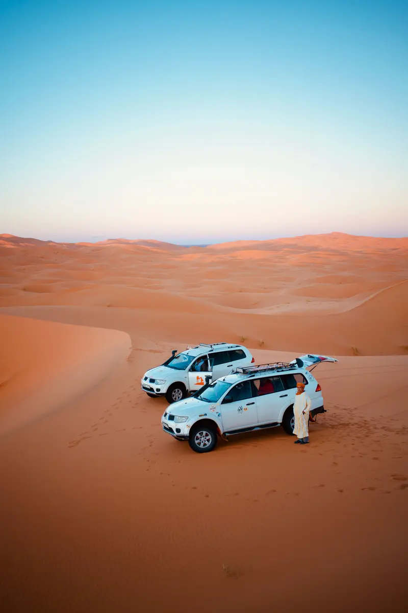 Deux 4x4 blancs stationnés dans les dunes, avec un homme à côté du véhicule au premier plan