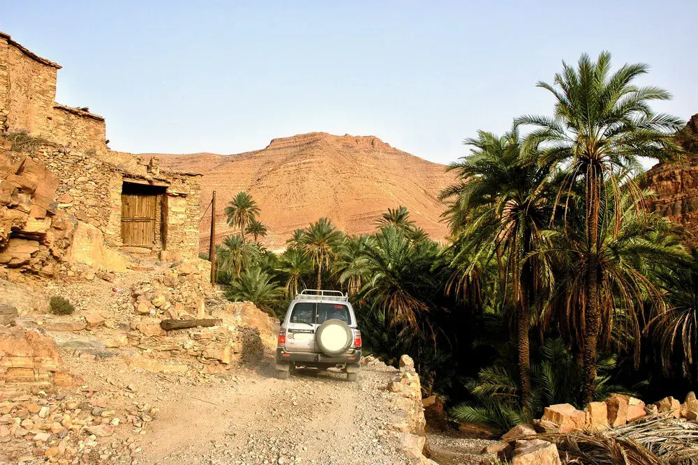 Un 4x4 sur une piste entre maisons en terre et palmiers
